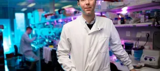 Professor Steve Pollard wearing a white lab coat, standing in the lab