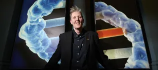 Professor Susan Rosser poses in front of an image render of a DNA molecule