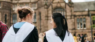 Two students in graduation gowns with their backs to the camera.