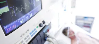 Close up of machines monitoring heart rate with man in bed in intensive care in background out of focus
