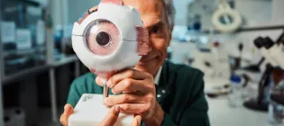 A researcher from the University of Edinburgh sitting in a lab holding a model of an eye
