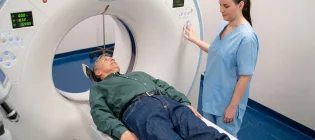 Older male patient on a CT scan machine in a hospital with a nurse in blue scrubs operating the equipment