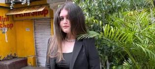 A student stands outside in front of a shop and fern plant.