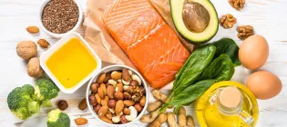 Keto diet food products displayed on a white wooden table. Salmon, olive oil, avocado, eggs, nuts and vegetables.