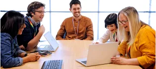 A group of four colleagues sit around a laptop laughing