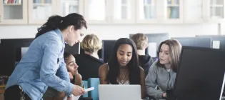 Mature teacher assisting female students using laptop in computer lab at high school - stock photo
