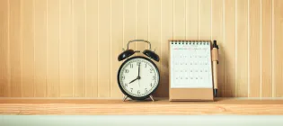 Image of an analogue alarm clock and calendar on a shelf