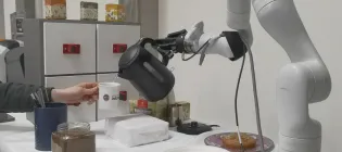 Coffee-making robot pours water from a kettle into a cup held by a person