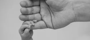 A baby's hand is seen gripping its mother's little finger