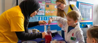 A festival volunteer helps a young boy perform a simple scientific experiment at the Edinburgh Science Festival