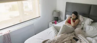 A teenage girl lies in bed looking out of the window