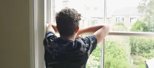 Teenage boy wearing dark t shirt looking out of bedroom window