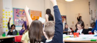 Two young students raise their hands in a classroom at IntoUniversity's centre inCraigmillar, Edinburgh