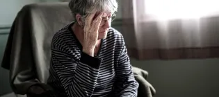 An elderly woman at home looking worried with her head in her hands