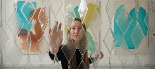 An ECA graduate approaches a sculpture that they designed made of glass and steel.