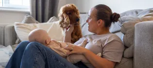 Mother sat in the floor holding newborn baby, with family dog watching nearby