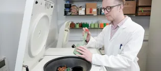 A man in a laboratory wearing a white coat transferring liquid between two containers