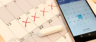 Image of a tampon and smartphone calendar on top of a paper calendar depicting menstrual cycle