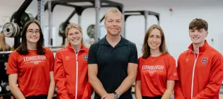 Sir Chris Hoy pictured centre, with four sports scholars wearing red University of Edinburgh sportwear