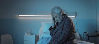 An elderly man sitting in a hospital bed at night and touching his head