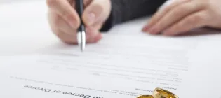  A person signs a divorce document. Two gold wedding rings are on the document