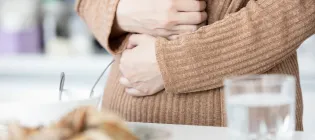 Close up of woman wearing beige jumper holding stomach