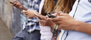 Group of four teenagers standing a line looking at mobile phones