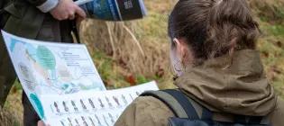 student in a field reading maps