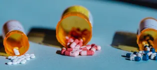 Three containers lie open on a table with pills spilling out of them