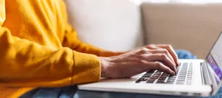 person in a yellow jumper typing on a keyboard