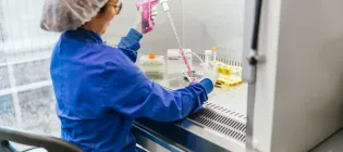 A female scientist in protective gear works with a pipette inside a biosafety cabinet, conducting cell culture experiments in a laboratory setting
