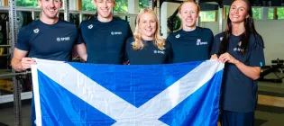 A group of swimmers from the University stand in a group holding a Scottish flag