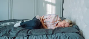 A woman in pain lying on bed and holding her stomach.