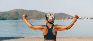 Senior woman pictured from behind exercising her back outdoors in a park
