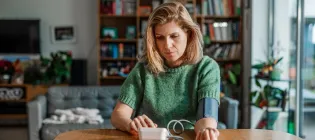 White middle-aged woman wearing short sleeved green jumper measuring her blood pressure at home
