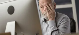Older man looking tired in front of a computer, rubbing his eyes. 