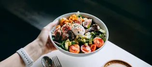 Close up of woman's hand holding a bowl of fresh, healthy food.