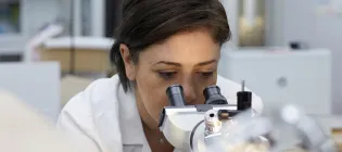 Female scientist wearing white lab coat looking down a microscope