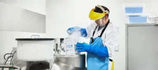 Male scientist examining frozen medicines in freezer. Researcher is working at laboratory. He is wearing protective mask.