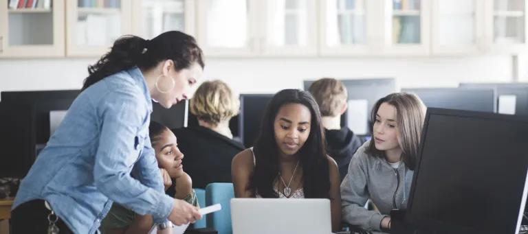 Mature teacher assisting female students using laptop in computer lab at high school - stock photo