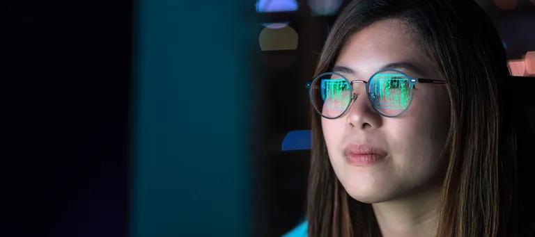 A woman looking at a screen with data reflected in her glasses