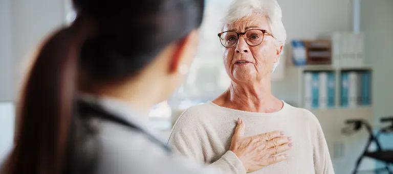 Older woman with her palm on her chest and speaking to medical professional