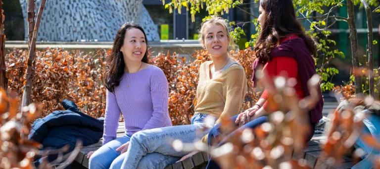 three students sitting outside talking looking happy