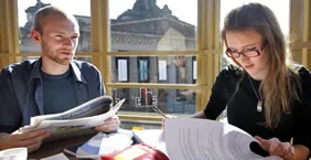 Two students sitting in a cafe looking through notes and papers.