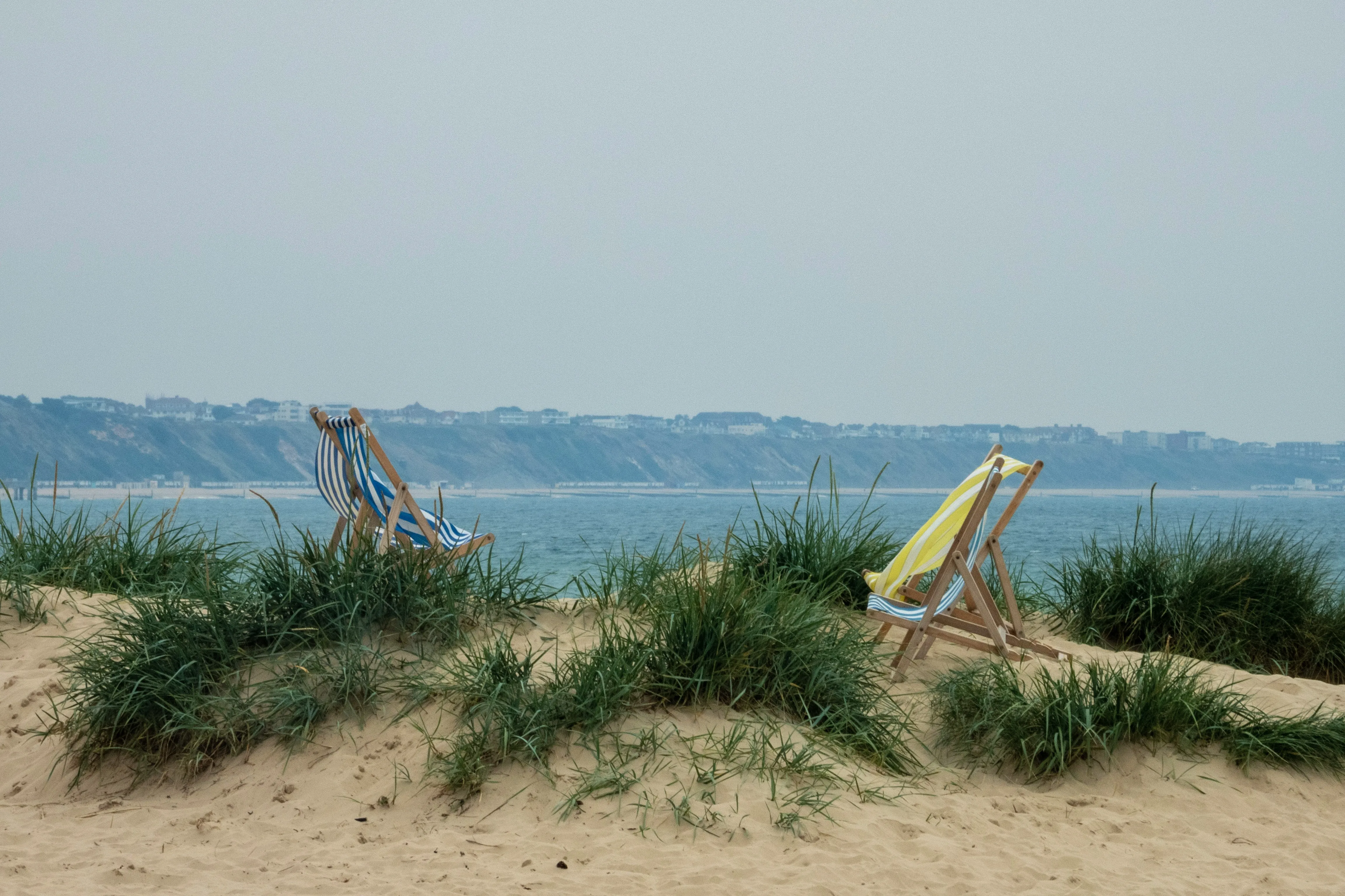 Two empty deckchairs overlook the sea on a sandy beach.