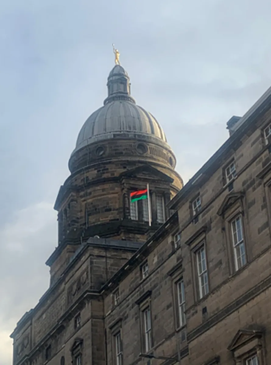 A red, green and black striped flag, flying on the roof of the University building, Old College