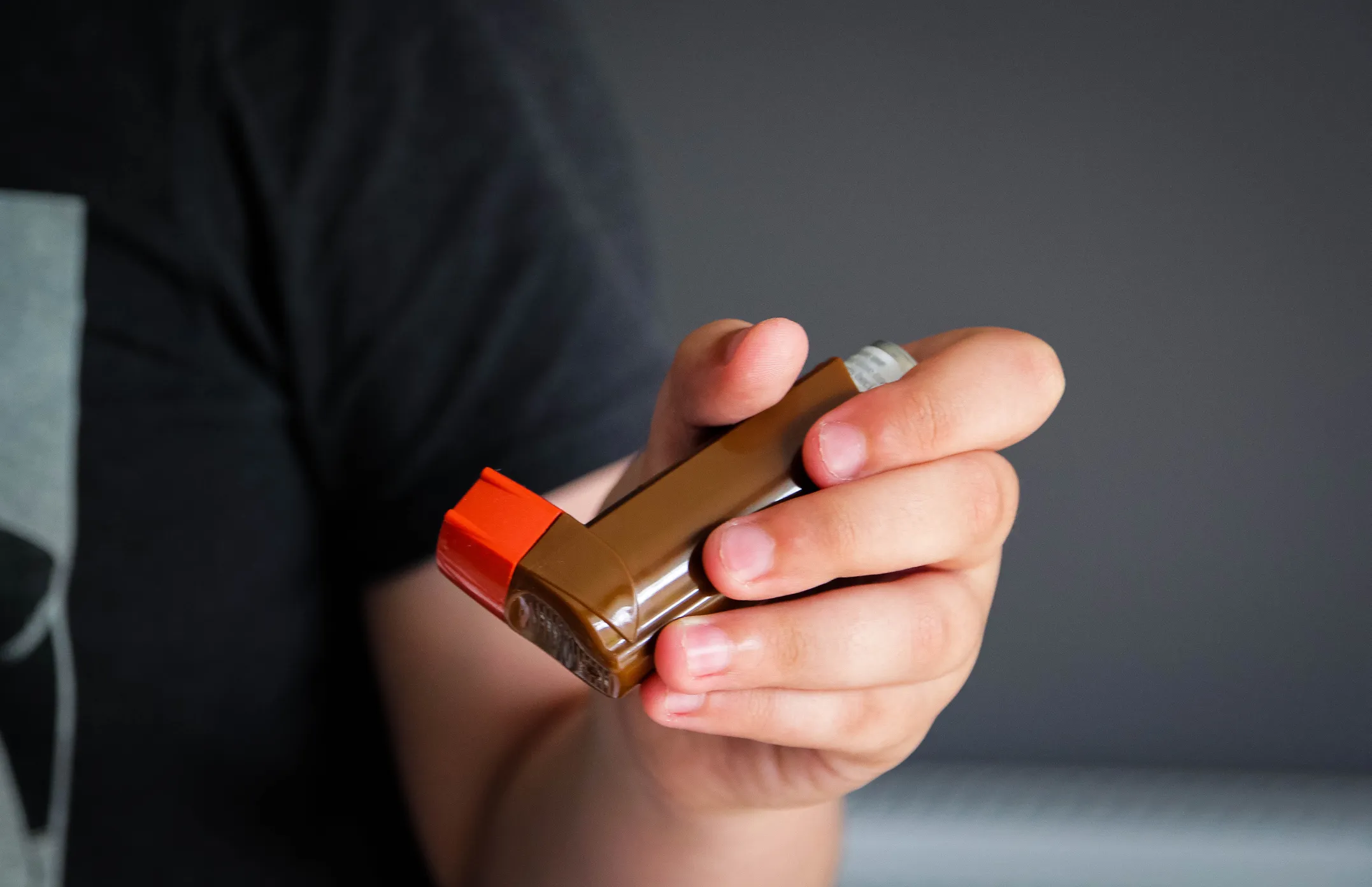 A photo of a child's hand holding a brown asthma inhaler