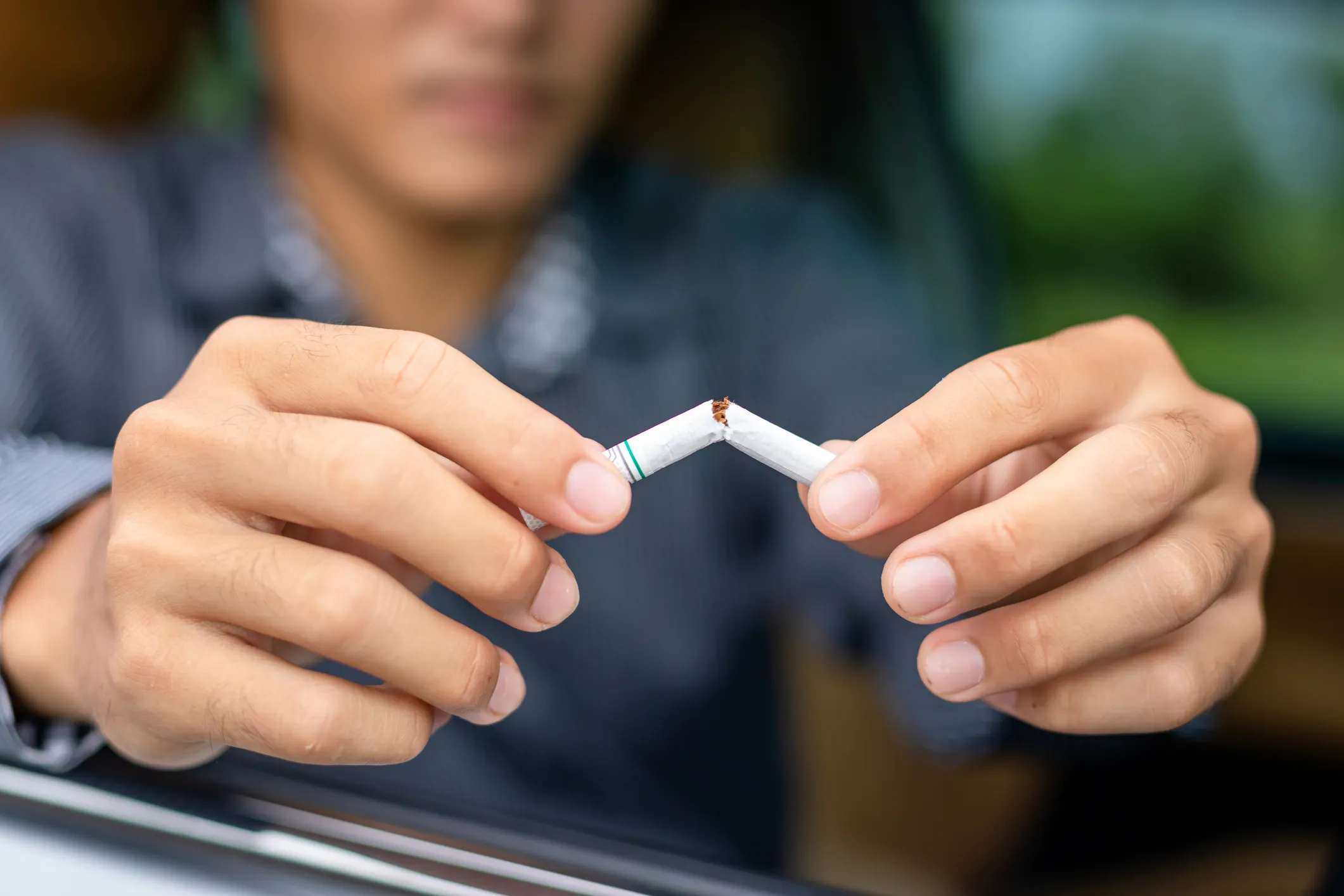 A man sitting in car with the window down snapping a cigarette in half