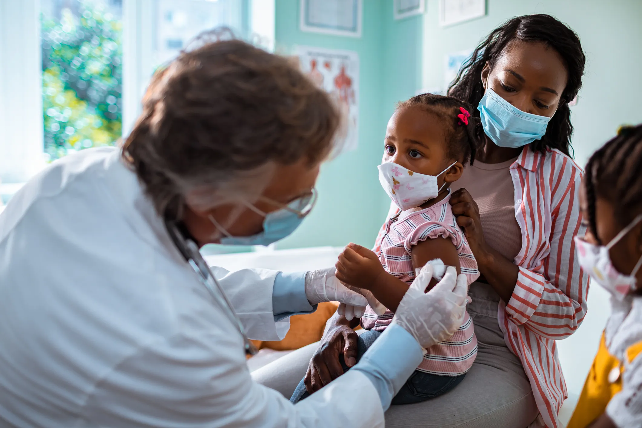 A photo of a mother and two children in a doctor's office where one child is being vaccinated 