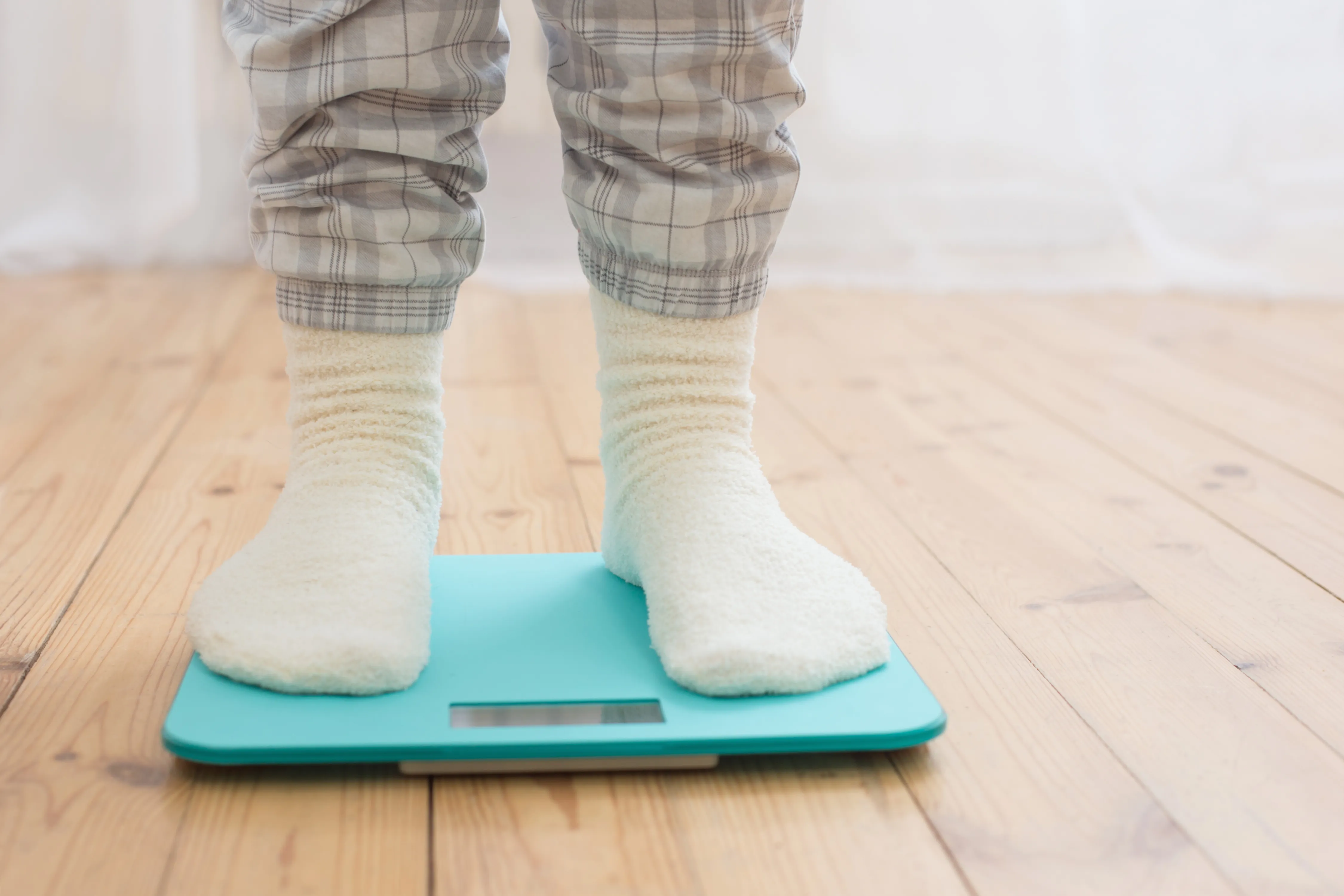 Female legs on electronic scales on wooden floor 